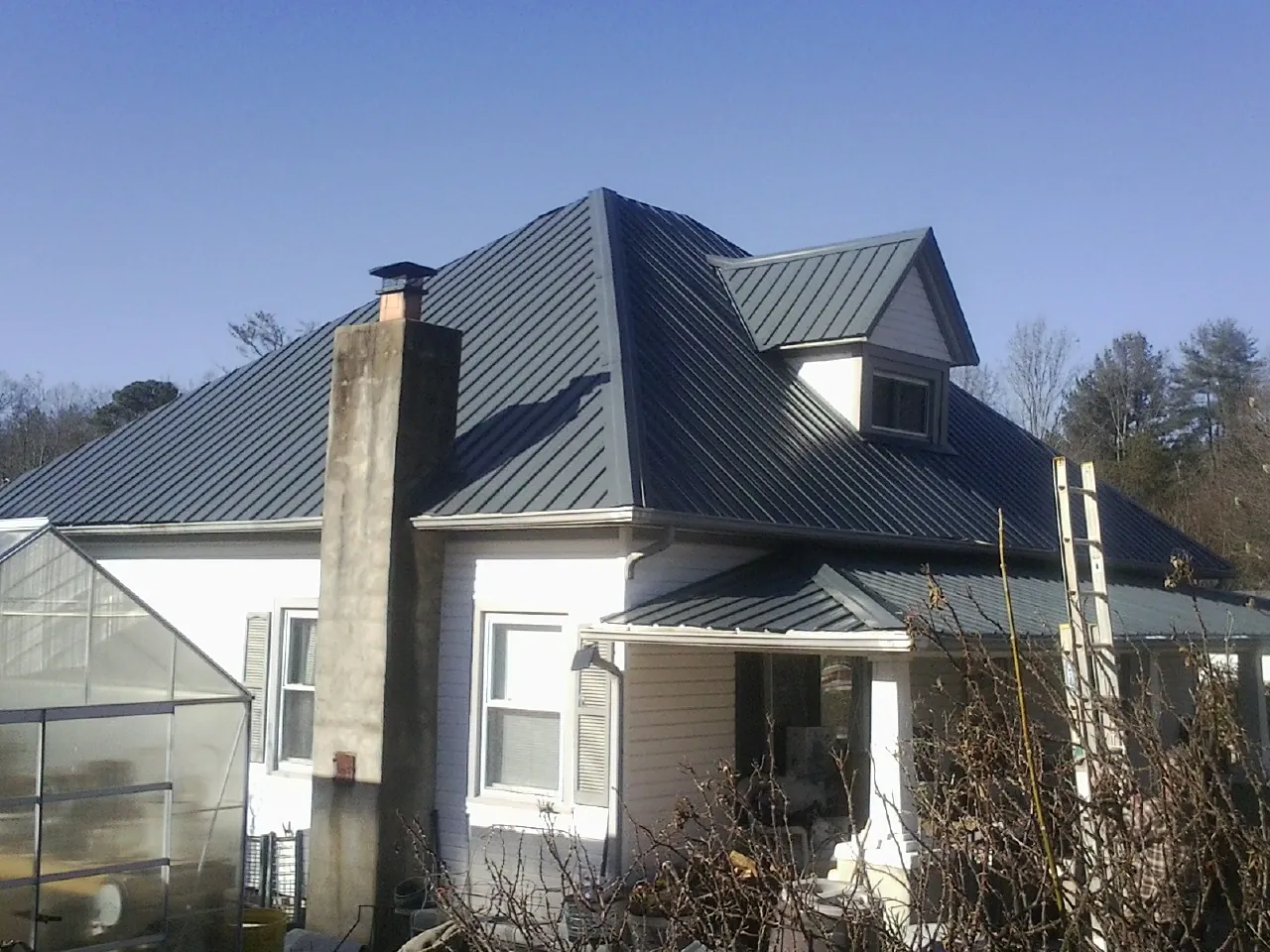 Dark blue standing seam metal roof on a white farmhouse with dormer — Slate & Tile Roof Repair by Roofing Brothers in Luthersburg