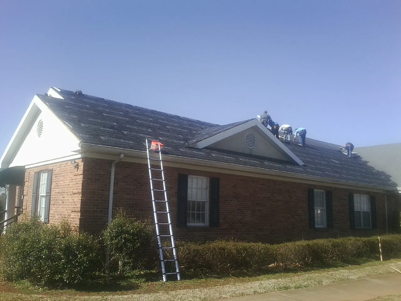 Crew tearing shingles off a brick ranch roof with a ladder set — Emergency Roof Repair work by our crew in Luthersburg