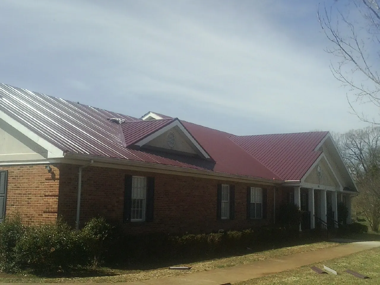 Red metal roof with gabled entries on a long brick building, from a Hail Damage Roof Repair job in Luthersburg