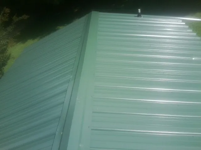 New green metal panels meeting at the ridge of a roof — Flat Roof Repair work by our crew in Luthersburg