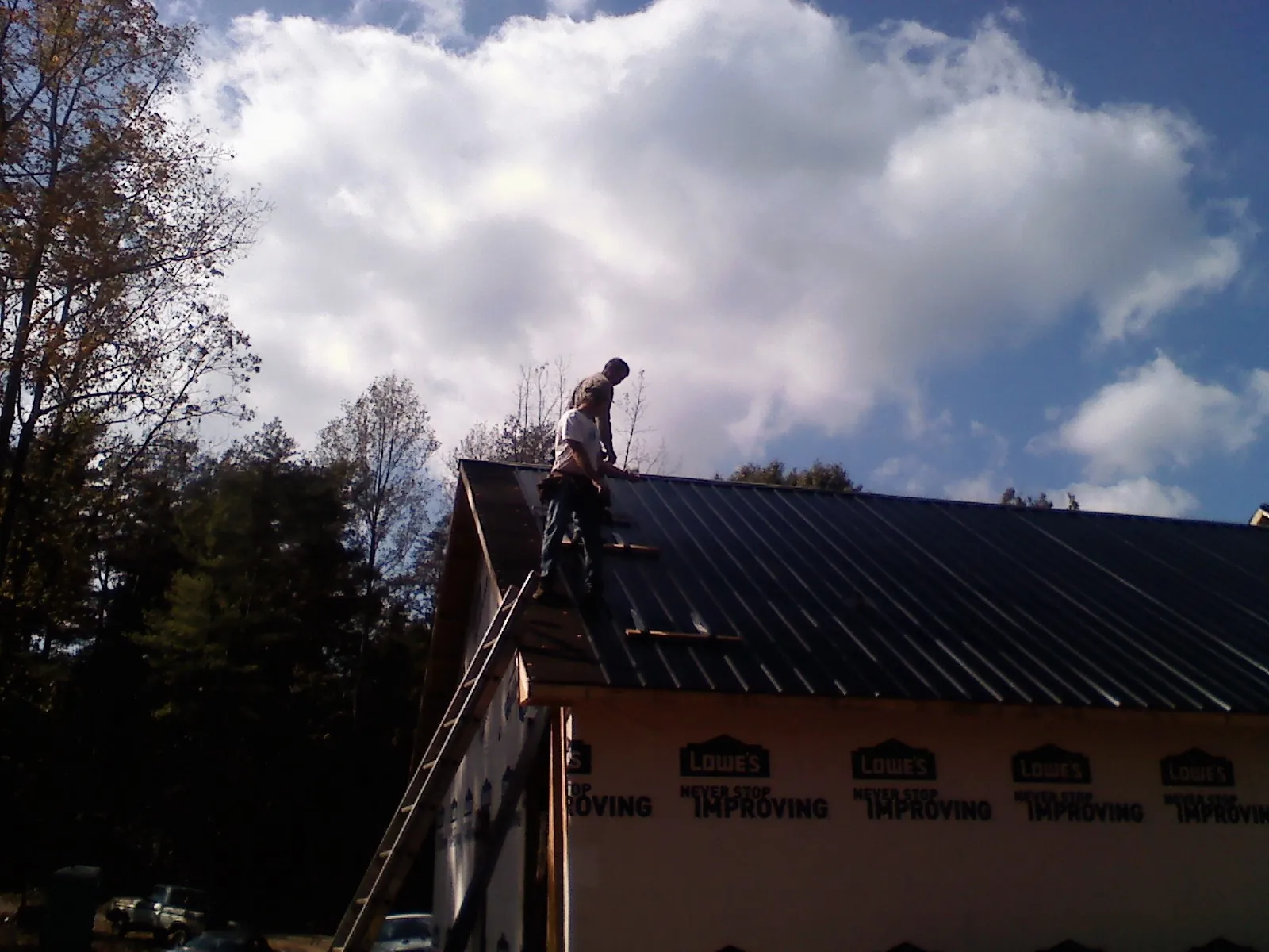 Roofer fastening dark metal panels high against a cloudy sky, from a Roof Inspection job in Luthersburg