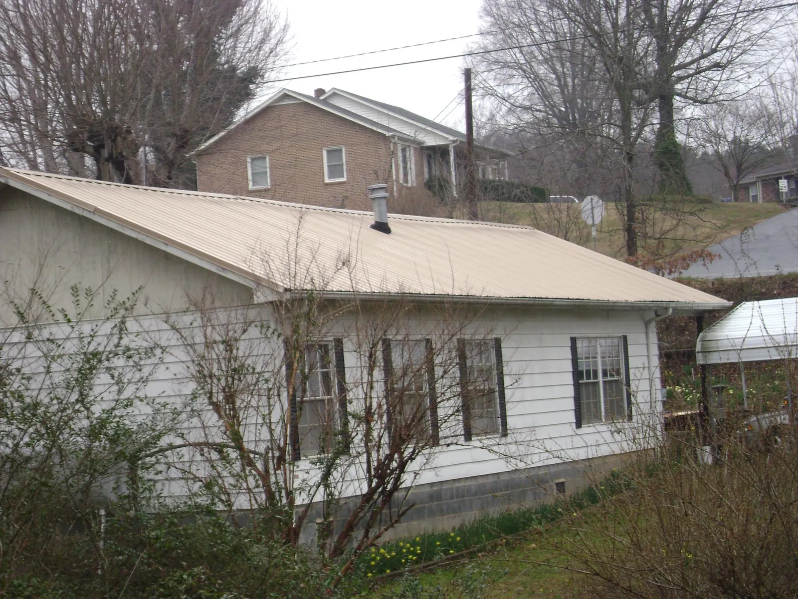 Tan metal roof on a white sided house set into a hillside — Commercial Roofing by Roofing Brothers in Luthersburg