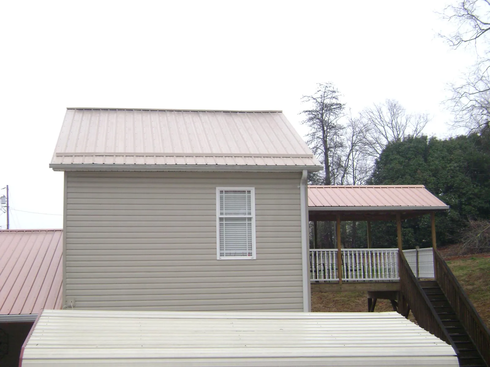 Tan metal roofs on a two story addition and attached porch, from a Roof Replacement job in Luthersburg